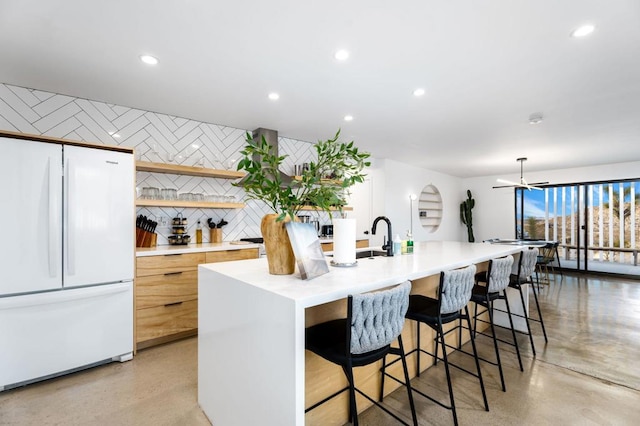 kitchen featuring a kitchen bar, hanging light fixtures, white refrigerator, an island with sink, and backsplash