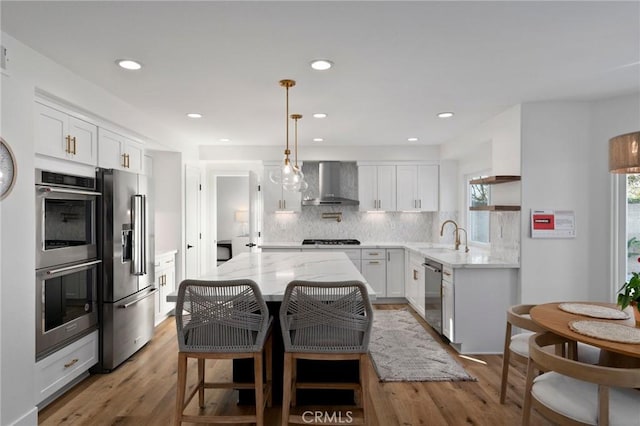 kitchen featuring white cabinetry, wall chimney range hood, stainless steel appliances, and a center island