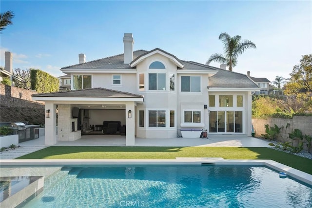 back of property with a fenced in pool, a patio, and an outdoor kitchen