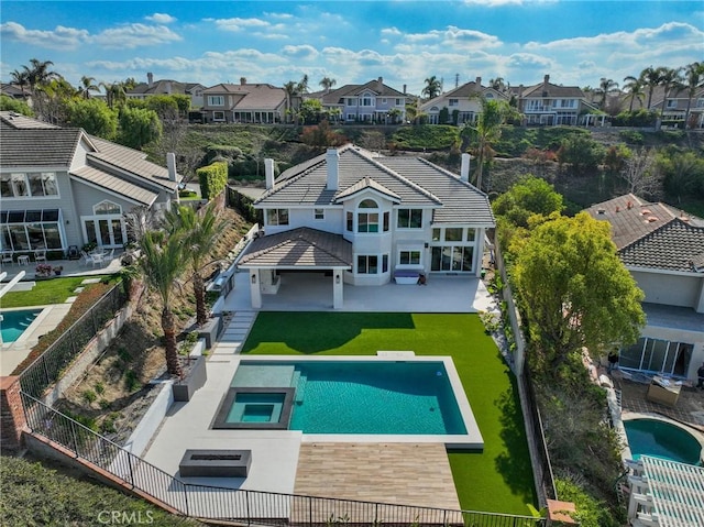 rear view of property featuring a swimming pool with hot tub, a patio, and a lawn