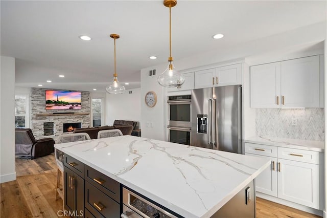 kitchen with hanging light fixtures, light stone countertops, white cabinets, and appliances with stainless steel finishes