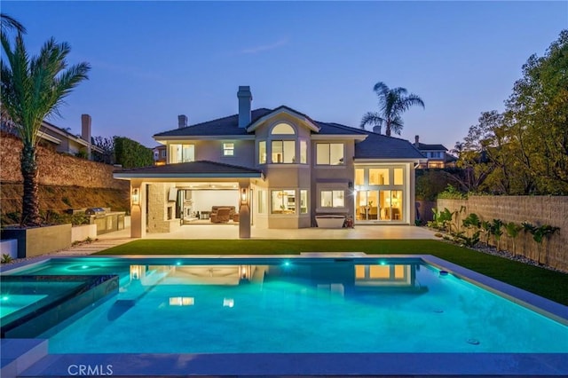 back house at dusk featuring an outdoor kitchen, a fenced in pool, and a patio