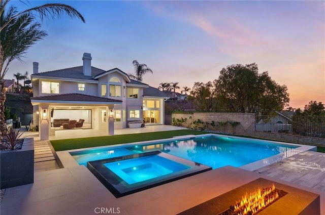 pool at dusk featuring an in ground hot tub, an outdoor fire pit, and a patio