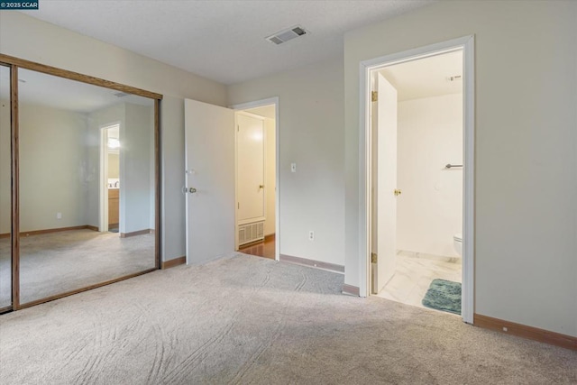 unfurnished bedroom with light carpet, ensuite bath, and a closet