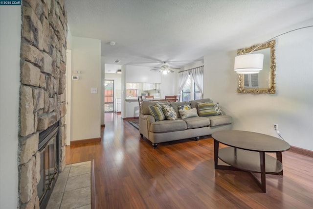 living room with a stone fireplace, wood-type flooring, a textured ceiling, and ceiling fan