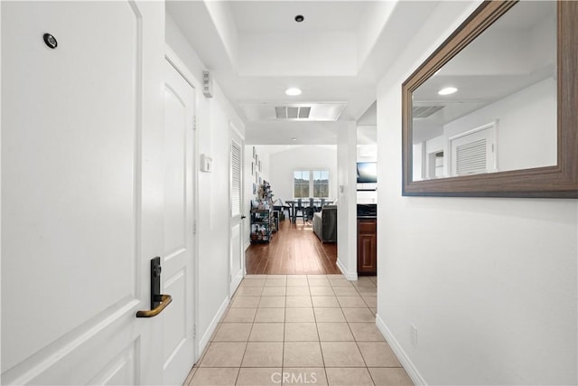 hall with a tray ceiling and light tile patterned floors