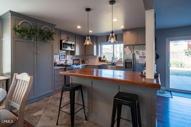 kitchen featuring butcher block countertops, hanging light fixtures, stainless steel appliances, and sink