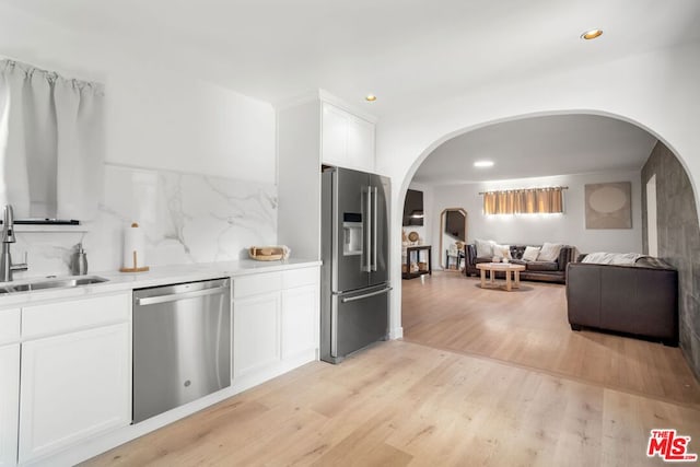 kitchen with sink, white cabinetry, light hardwood / wood-style flooring, stainless steel appliances, and decorative backsplash