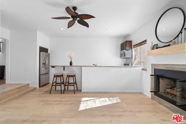 kitchen featuring ceiling fan, stainless steel appliances, a tiled fireplace, and light wood-type flooring