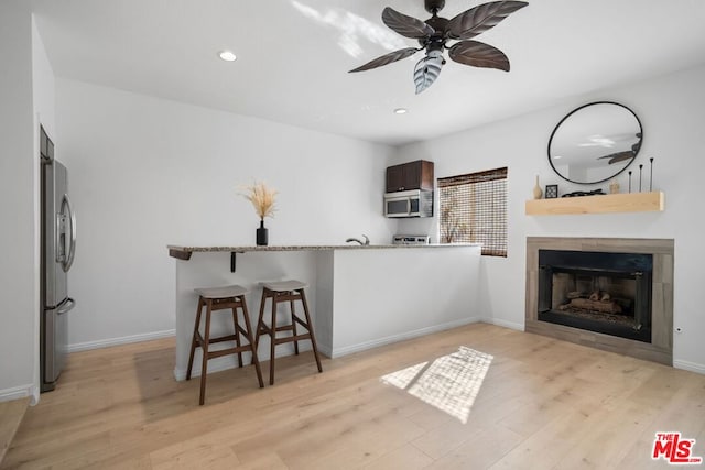 interior space with light wood-type flooring, appliances with stainless steel finishes, a kitchen breakfast bar, kitchen peninsula, and ceiling fan