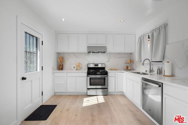 kitchen with wall chimney exhaust hood, sink, white cabinetry, appliances with stainless steel finishes, and backsplash