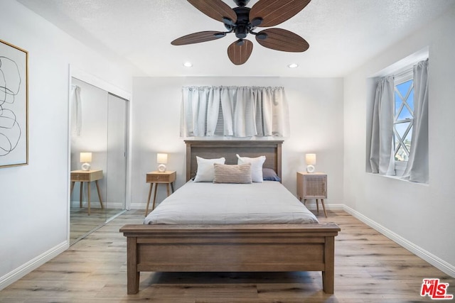 bedroom featuring ceiling fan, a closet, light hardwood / wood-style flooring, and a textured ceiling