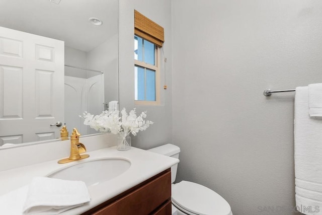 bathroom with walk in shower, vanity, and toilet