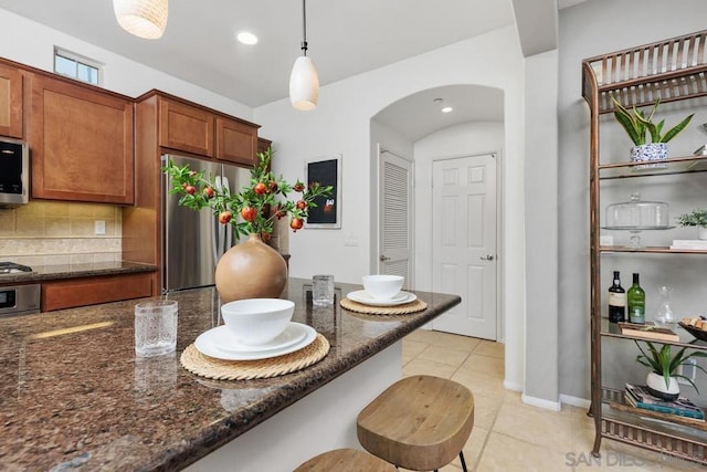 kitchen featuring decorative light fixtures, light tile patterned floors, appliances with stainless steel finishes, dark stone counters, and backsplash