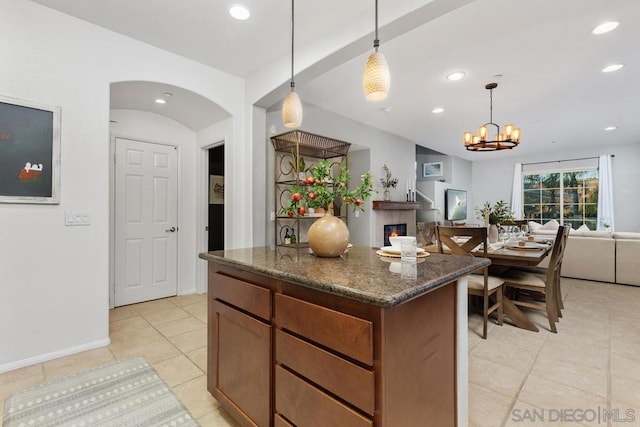 kitchen featuring pendant lighting, a fireplace, light tile patterned floors, and dark stone countertops