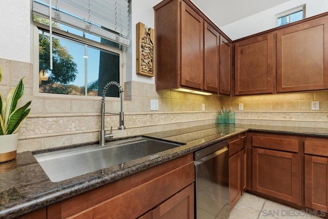 kitchen with dark stone countertops, dishwashing machine, sink, and a wealth of natural light