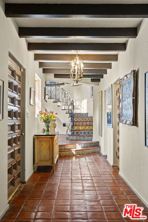 hallway featuring beam ceiling, dark tile patterned flooring, and an inviting chandelier