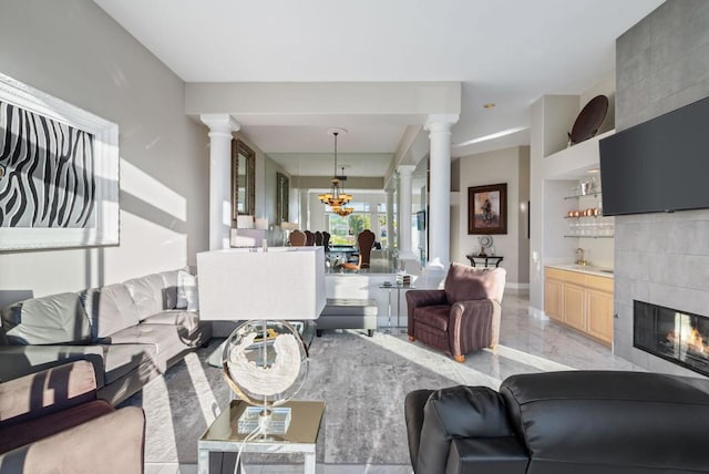 living room featuring ornate columns, a tile fireplace, an inviting chandelier, and built in shelves