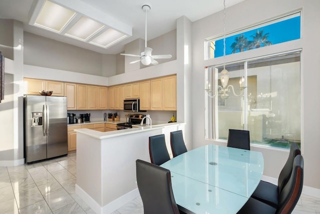 kitchen with ceiling fan, appliances with stainless steel finishes, a high ceiling, kitchen peninsula, and light brown cabinets