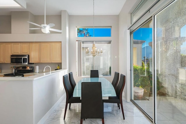 dining room with ceiling fan with notable chandelier and a high ceiling