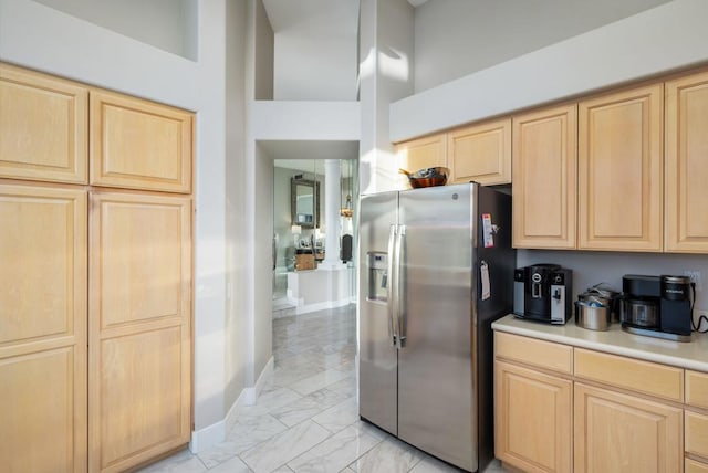 kitchen featuring light brown cabinetry, a towering ceiling, and stainless steel fridge