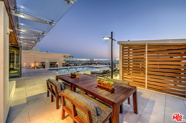 patio terrace at dusk featuring a community pool