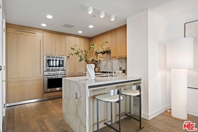 kitchen with light brown cabinetry, dark hardwood / wood-style floors, stainless steel appliances, and kitchen peninsula