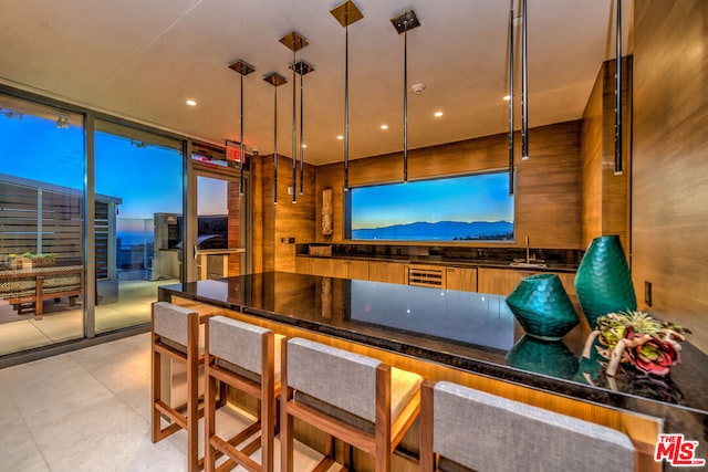 bar featuring a wall of windows, decorative light fixtures, sink, and wood walls