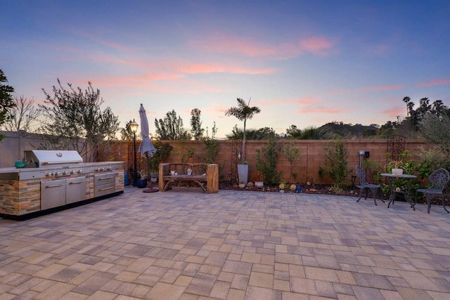 patio terrace at dusk featuring area for grilling and an outdoor kitchen