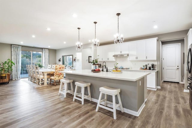 kitchen with pendant lighting, white cabinetry, a kitchen breakfast bar, light hardwood / wood-style floors, and a center island with sink