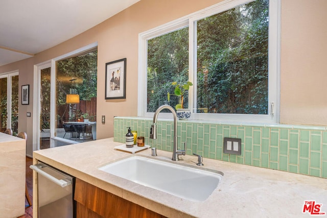 kitchen with stainless steel dishwasher, light stone countertops, sink, and decorative backsplash