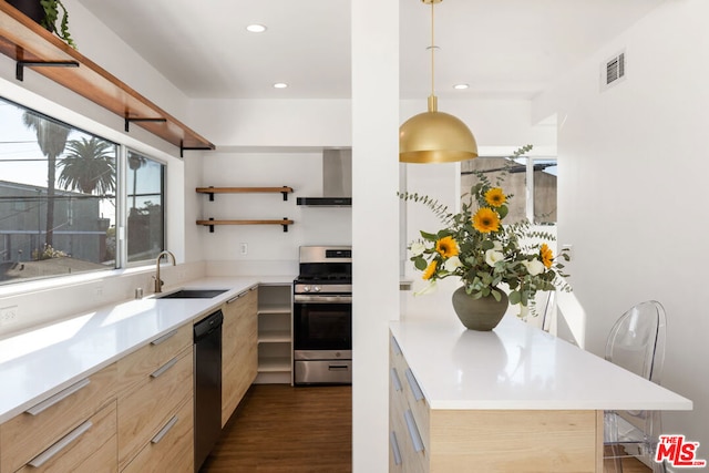 kitchen featuring gas range, wall chimney range hood, light brown cabinetry, and decorative light fixtures