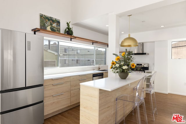 kitchen with sink, a breakfast bar area, a center island, stainless steel appliances, and wall chimney exhaust hood