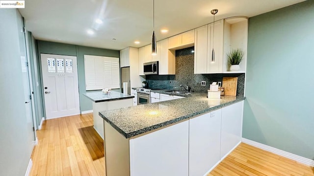 kitchen with appliances with stainless steel finishes, pendant lighting, white cabinetry, decorative backsplash, and kitchen peninsula