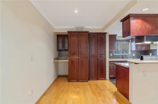 kitchen with tasteful backsplash, sink, crown molding, wall chimney range hood, and light hardwood / wood-style flooring