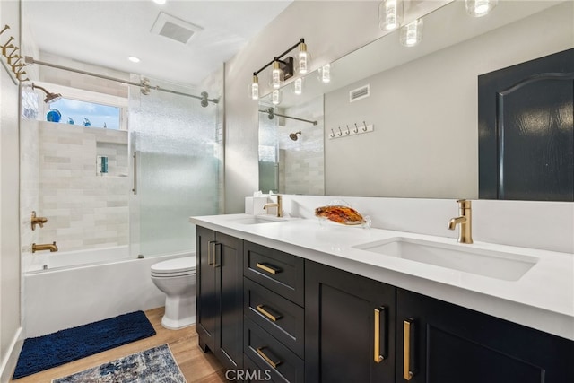 full bathroom featuring hardwood / wood-style flooring, vanity, shower / bath combination with glass door, and toilet