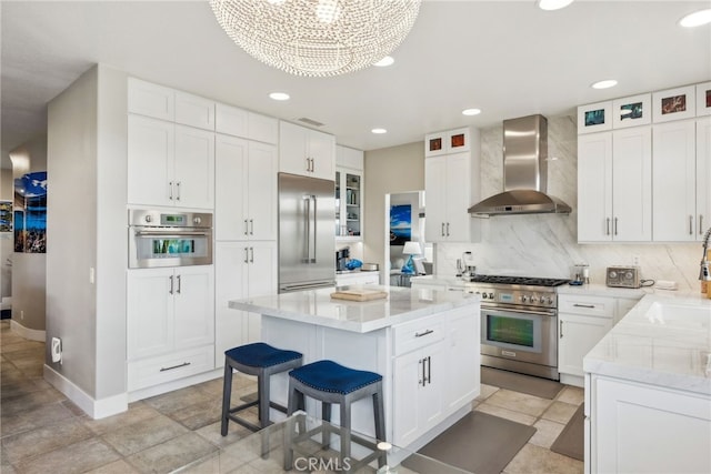 kitchen featuring wall chimney range hood, white cabinetry, backsplash, a center island, and high quality appliances