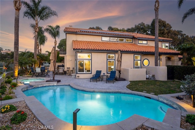 back house at dusk with a swimming pool with hot tub and a patio