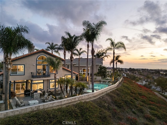 back house at dusk featuring a patio and a balcony