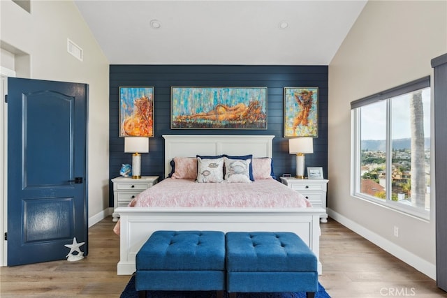 bedroom featuring vaulted ceiling, wood walls, and light hardwood / wood-style flooring