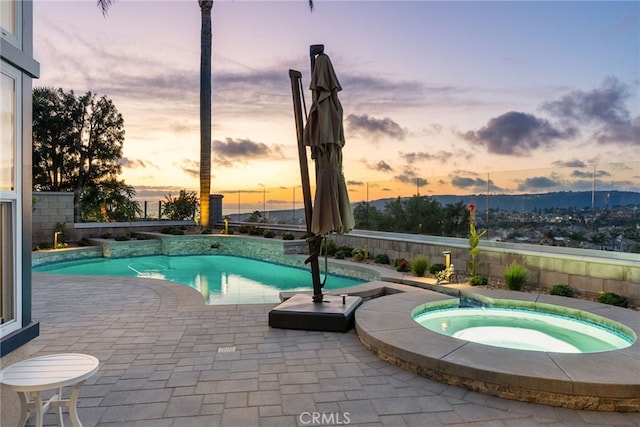 pool at dusk with an in ground hot tub and a patio