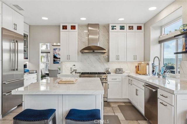 kitchen with sink, a breakfast bar, white cabinetry, high end appliances, and wall chimney exhaust hood