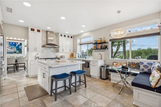 kitchen featuring white cabinetry, decorative light fixtures, wall chimney exhaust hood, and a kitchen island