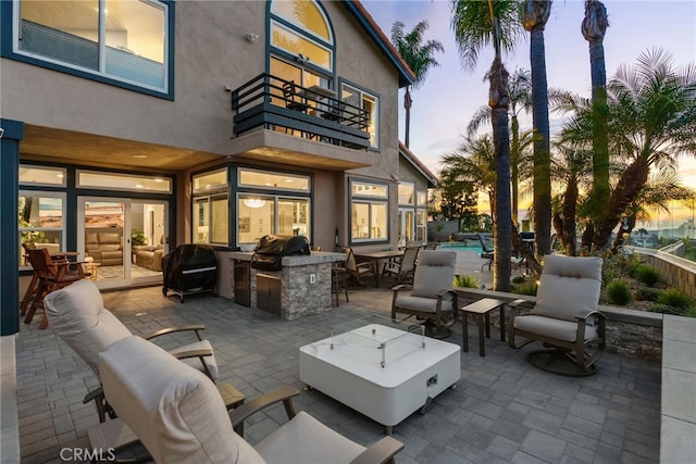 patio terrace at dusk featuring a balcony, grilling area, exterior bar, and exterior kitchen