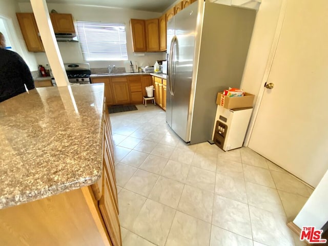 kitchen with appliances with stainless steel finishes, sink, light tile patterned floors, and light stone counters