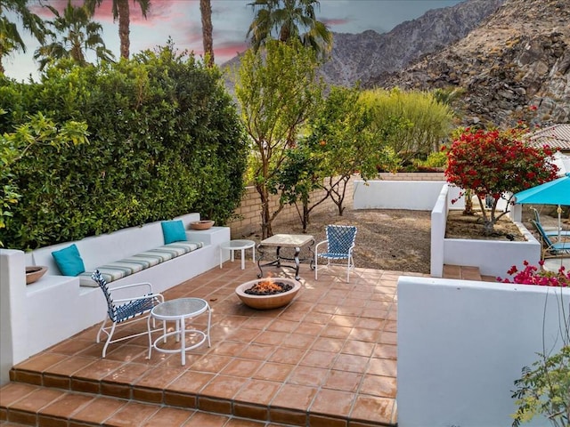 patio terrace at dusk featuring a mountain view and an outdoor living space with a fire pit