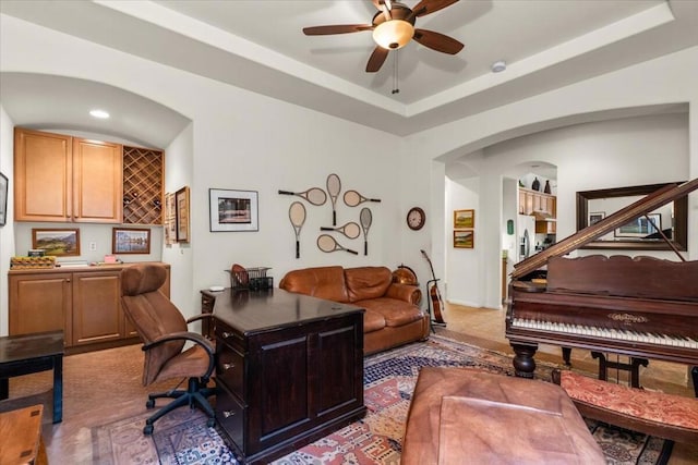 carpeted home office featuring ceiling fan and a tray ceiling