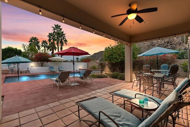 patio terrace at dusk with ceiling fan and a fenced in pool