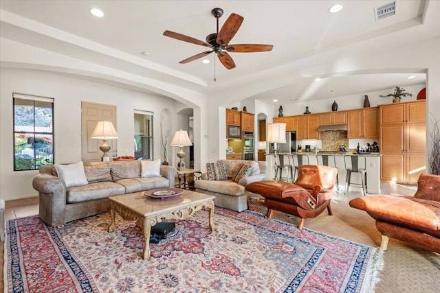 living room featuring a raised ceiling, light tile patterned floors, and ceiling fan