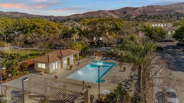 pool at dusk featuring a mountain view, a patio area, and a pergola